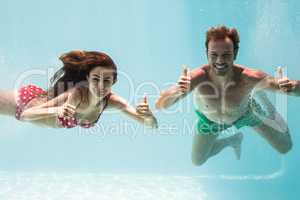 Smiling couple showing thumbs up while swimming