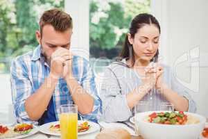 Couple praying while sitting at dining table