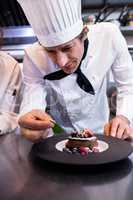 Male chef garnishing a dessert with a mint leaf on counter