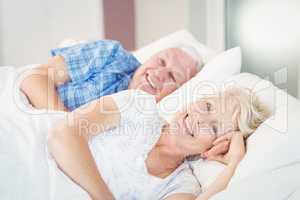 Portrait of happy senior woman resting besides man on bed