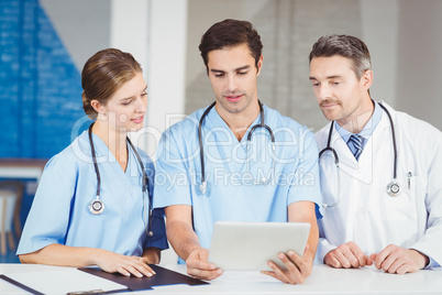 Doctor and colleagues using digital tablet while standing at des