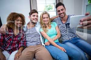 Multi-ethnic friends taking selfie while sitting on sofa