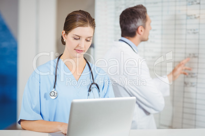 Female doctor working on laptop with colleague pointing at chart