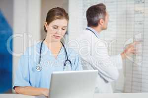 Female doctor working on laptop with colleague pointing at chart