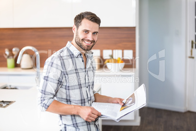 Man holding newspaper while leaning on kitchen counter