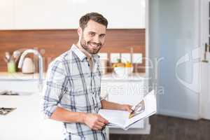 Man holding newspaper while leaning on kitchen counter