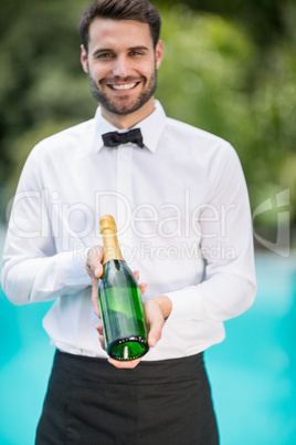 Portrait of smiling waiter holding champagne bottle