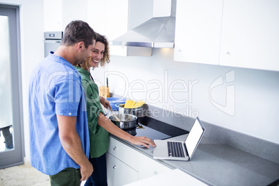 Couple working on laptop while cooking