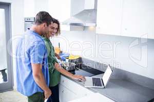 Couple working on laptop while cooking