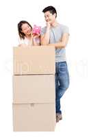 Young couple leaning on cardboard boxes and looking at piggy ban
