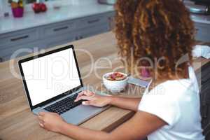 Woman using laptop while sitting by table