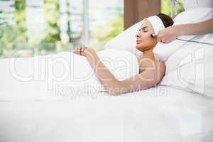 Woman relaxing on bed while receiving facial massage