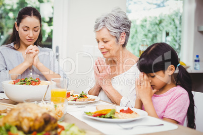Mother and daughter with granny praying at dining table