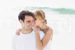 Young woman whispering in mans ears on the beach
