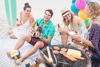 Group of friends with drinks and guitar sitting next to a barbec