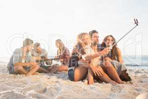 Smiling friends sitting on sand singing and taking selfies