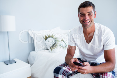 Portrait of man sitting on bed and typing a text message on phon