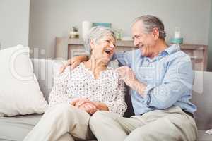 Romantic senior couple laughing while sitting on sofa