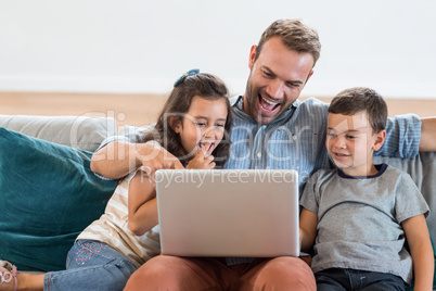 Father sitting with son and daughter and using laptop