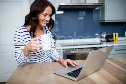 Smiling young woman working on laptop while holding coffee mug Smiling young woman working on laptop while holding coffee mug