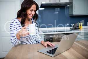 Smiling young woman working on laptop while holding coffee mug