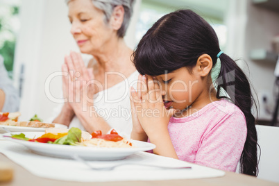 Granny and granddaughter praying at dining table