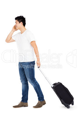 Young man talking on mobile phone while walking with suitcase