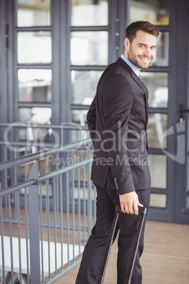 Handsome businessman walking with luggage in office