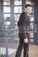 Handsome businessman walking with luggage in office