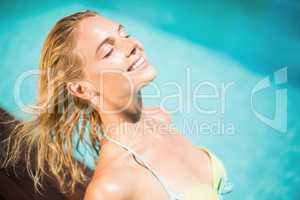 Happy woman in bikini sitting by pool side