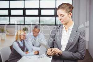 Businesswoman using digital tablet while colleague in background