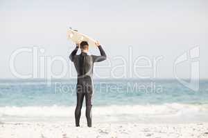 Rear view of man holding surfboard over head