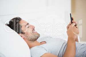 Young man smiling while using mobile phone on bed