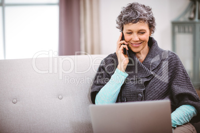 Mature woman with laptop talking on mobile phone at home