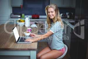 Beautiful young woman smiling while using laptop at table