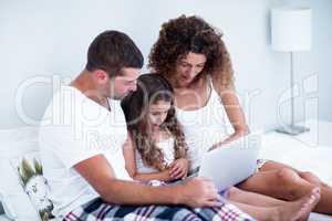 Couple using laptop with their daughter on bed