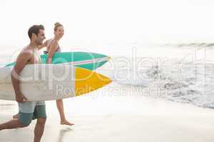 Couple with surfboard running on the beach