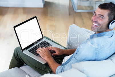 Portrait of young man listening to music while using laptop