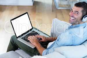 Portrait of young man listening to music while using laptop