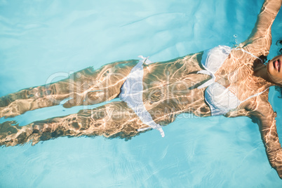 Beautiful woman in white bikini floating in swimming pool