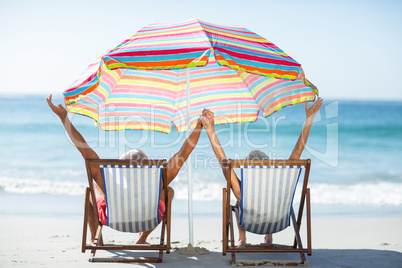 Cute mature couple raising arms on deckchairs