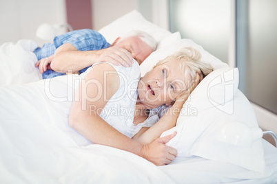 Shocked senior woman sleeping besides man on bed