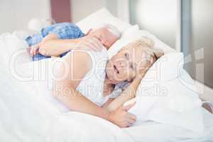 Shocked senior woman sleeping besides man on bed