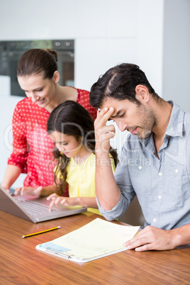 Daughter and mother working on laptop with tensed father sitting