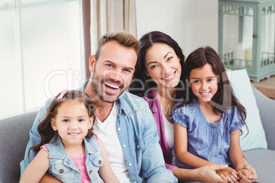 Parents smiling while sitting with daughters on sofa