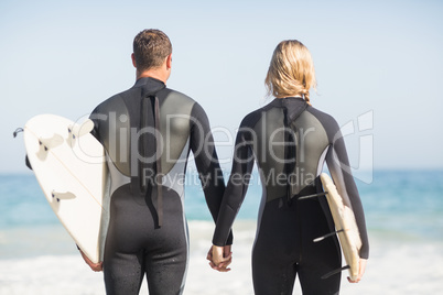 Rear view of couple with surfboard holding hand on the beach