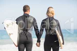 Rear view of couple with surfboard holding hand on the beach