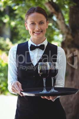 Smiling waitress holding a tray with glasses of red wine