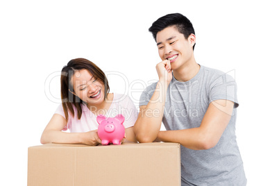 Young couple looking at piggy bank on cardboard box
