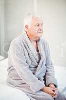 Thoughtful senior man in bathrobe sitting on bed